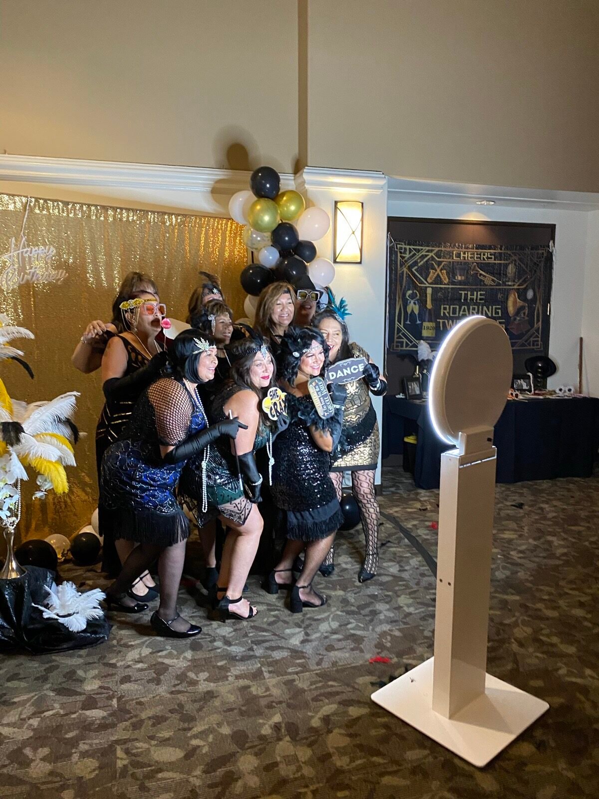 Guests in 1920s flapper outfits posing next to the selfie photo booth at a Roaring Twenties party