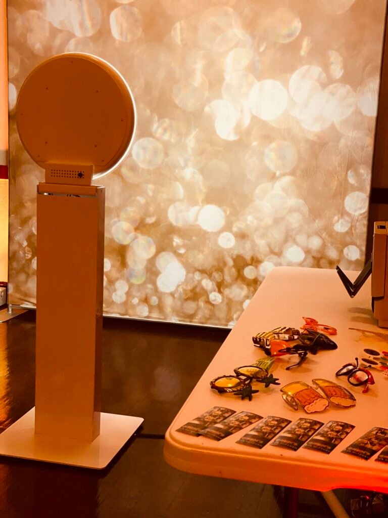 Selfie photo booth with a gold sparkle backdrop and props table